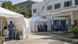 Carpas de atención médica en el patio de un hospital rural, con personal de salud y pacientes.