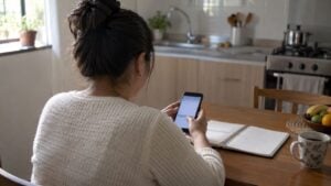 Una trabajadora independiente revisa en su celular un pago de aportes en la mesa de su cocina.
