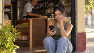 Una mujer revisa una aplicación en su celular en la puerta de una tienda de barrio.