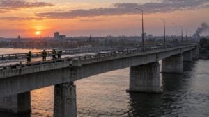 Bomberos revisan la calzada de un gran puente sobre un río ancho al atardecer.