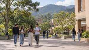 Estudiantes caminan por la plazoleta de un campus universitario de ladrillo con montañas al fondo.