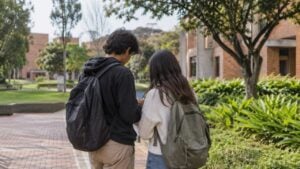 Dos estudiantes universitarios revisan un celular en el campus de una universidad pública.