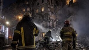 Rescatistas trabajan de noche frente a un edificio residencial destruido.