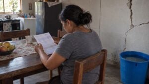 Una mujer revisa la factura del agua en una vivienda con grietas en la pared tras el terremoto.