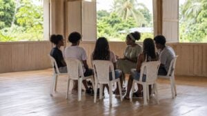 Jóvenes adultos conversan en círculo con una facilitadora en un salón comunitario del Pacífico.