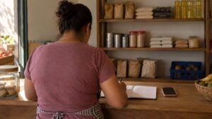 La dueña de una tienda de barrio revisa cuentas en el mostrador.