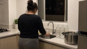 Una mujer llena botellas con agua del grifo en la cocina de su casa, de noche.