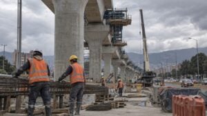Trabajadores con casco y chaleco en la obra de un viaducto elevado sobre una avenida de Bogotá.